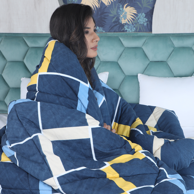 Woman wrapped in a blue and yellow patterned blanket sitting on a bed with a teal headboard.